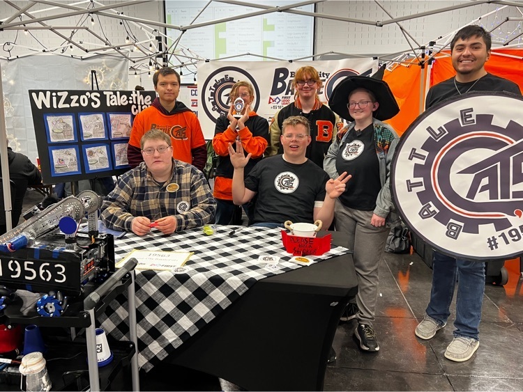 Team poses in front of black and white table cloth with a robot and paper shield and a shiny trophy 
